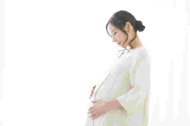 お腹を押さえながら微笑む妊婦