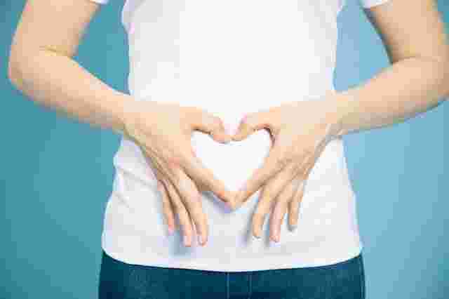 女性のお腹に前で手でハート