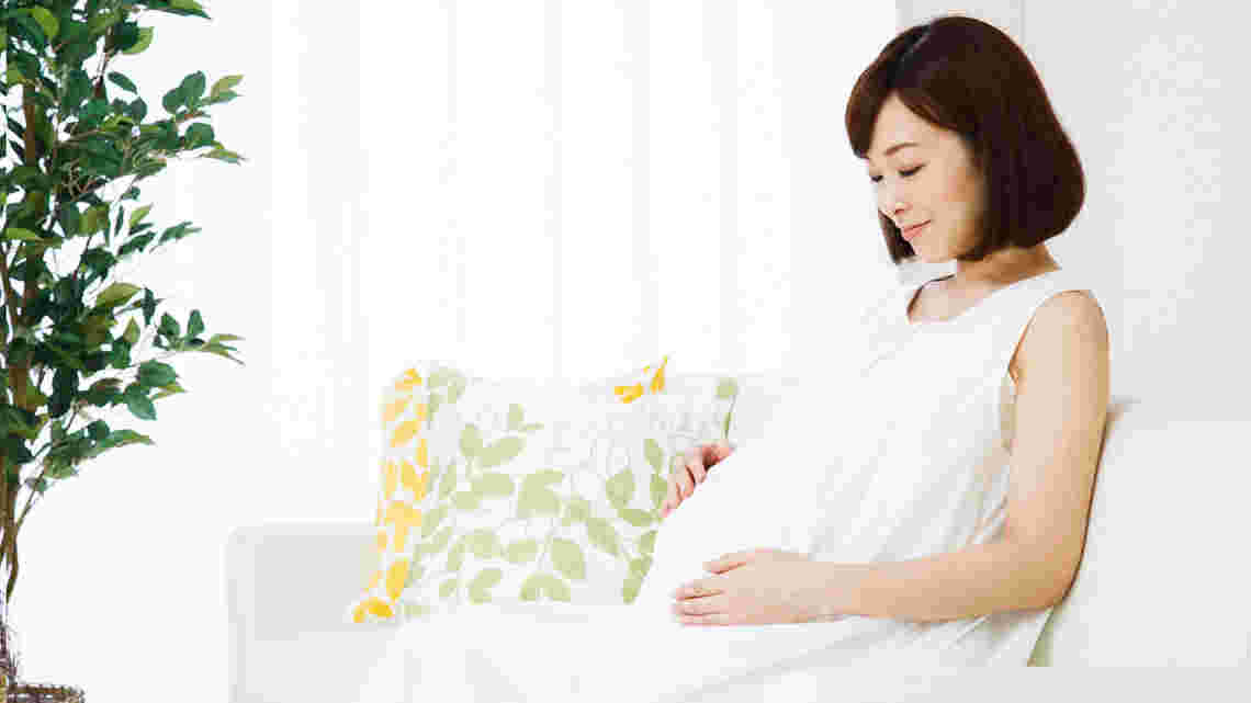 白い服を着た妊婦が座ってお腹に手を当てている様子