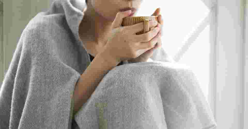毛布で体をつつみ、暖かい飲み物を飲む女性