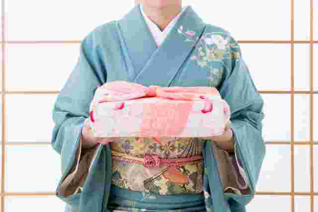 菓子折りを渡そうとする着物の女性