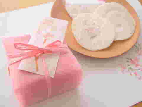桃色の和紙に包まれた箱の隣にお皿にのったさくらせんべい