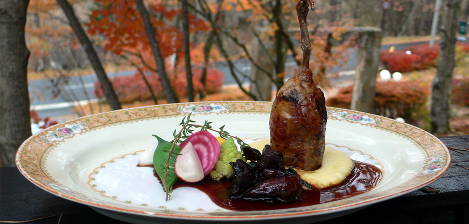 紅葉の背景と美しく盛られたフォンドジビエソースの肉料理の写真