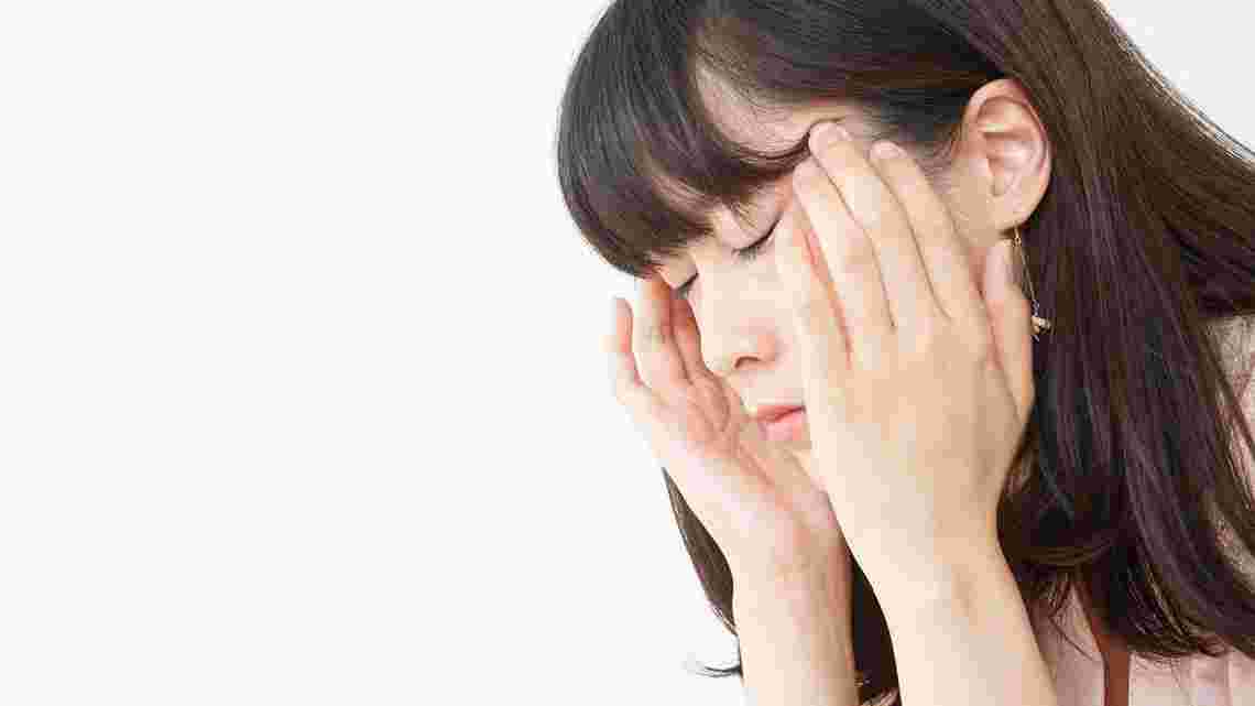 両手で頭を痛そうに押さえる女性