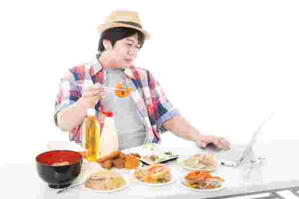 パソコンの前でたくさんの食べ物を食べている男性
