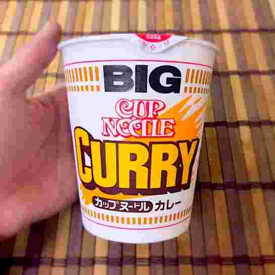 片手に持たれている細長型のカップ麺に描かれている英語カリーが大きい