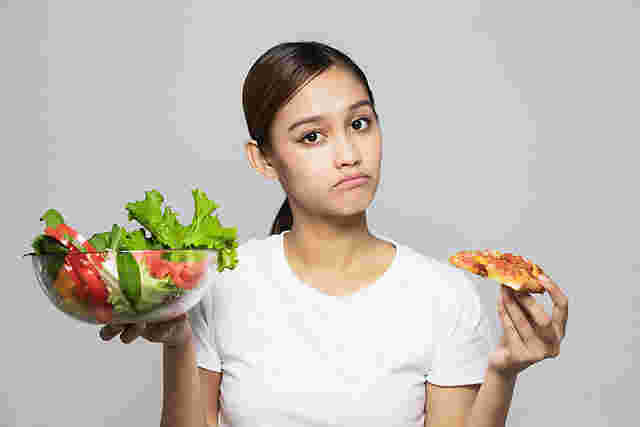 女性が左手にカットされたピザ、右手に大量の野菜が入ったボウルを持っている