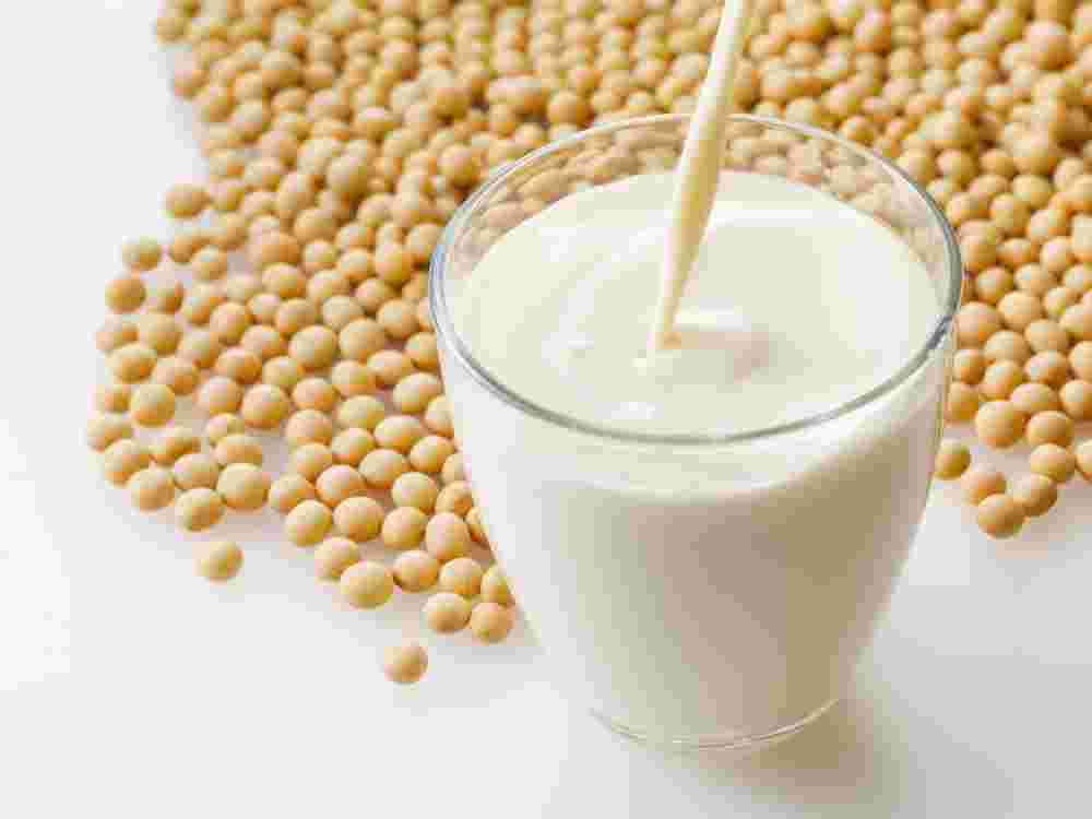 コップに注がれた豆乳と周りに散りばめられた大豆