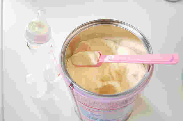缶入りの粉ミルクをスプーンですくっている横に哺乳瓶がある様子