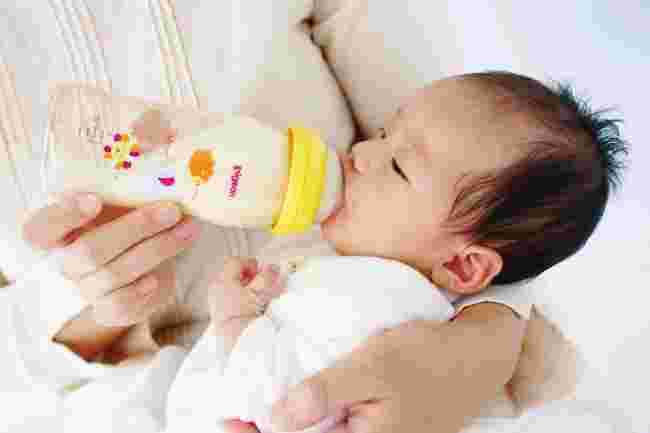 お母さんに抱かれながら哺乳瓶のミルクを飲む赤ちゃん