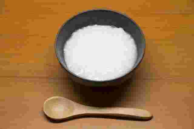 丸い茶碗におかゆが入っていてその下に木のスプーンが綺麗に置かれている