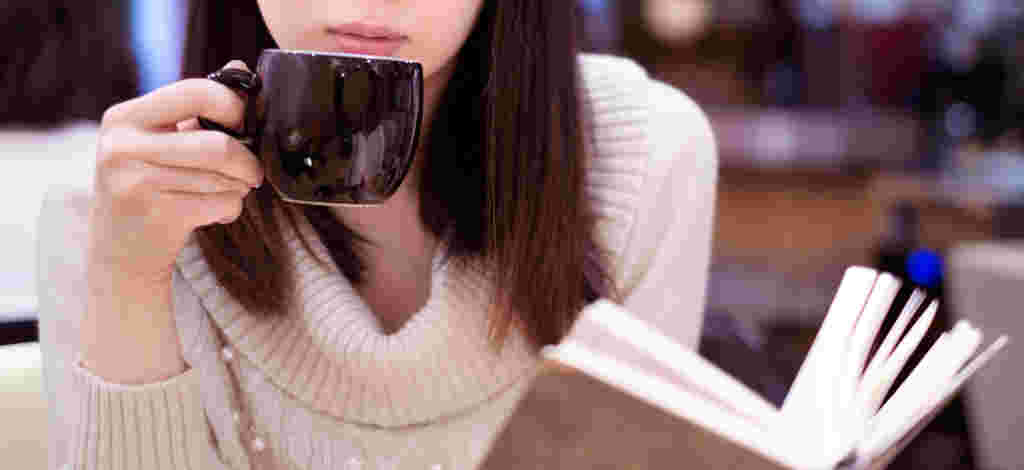 本を読みながらコーヒーを飲んでいる女性