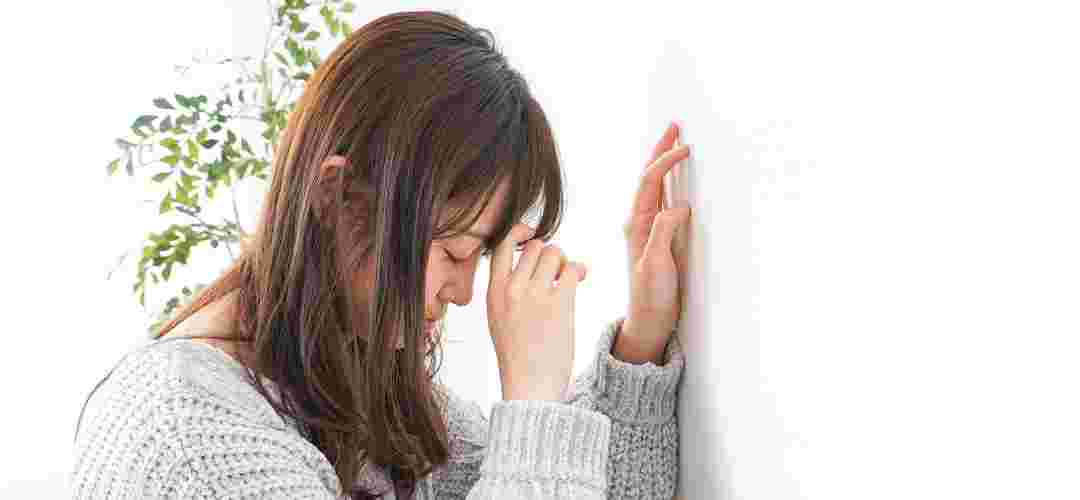 こめかみに手を当て壁にもたれかかる女性
