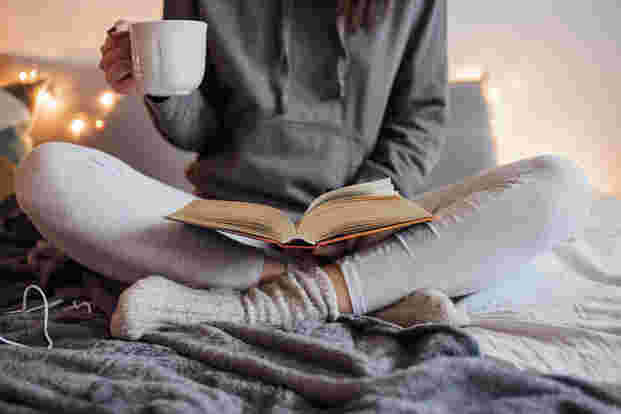 あぐらをかきながら温かい飲み物を飲みながら読書する女性