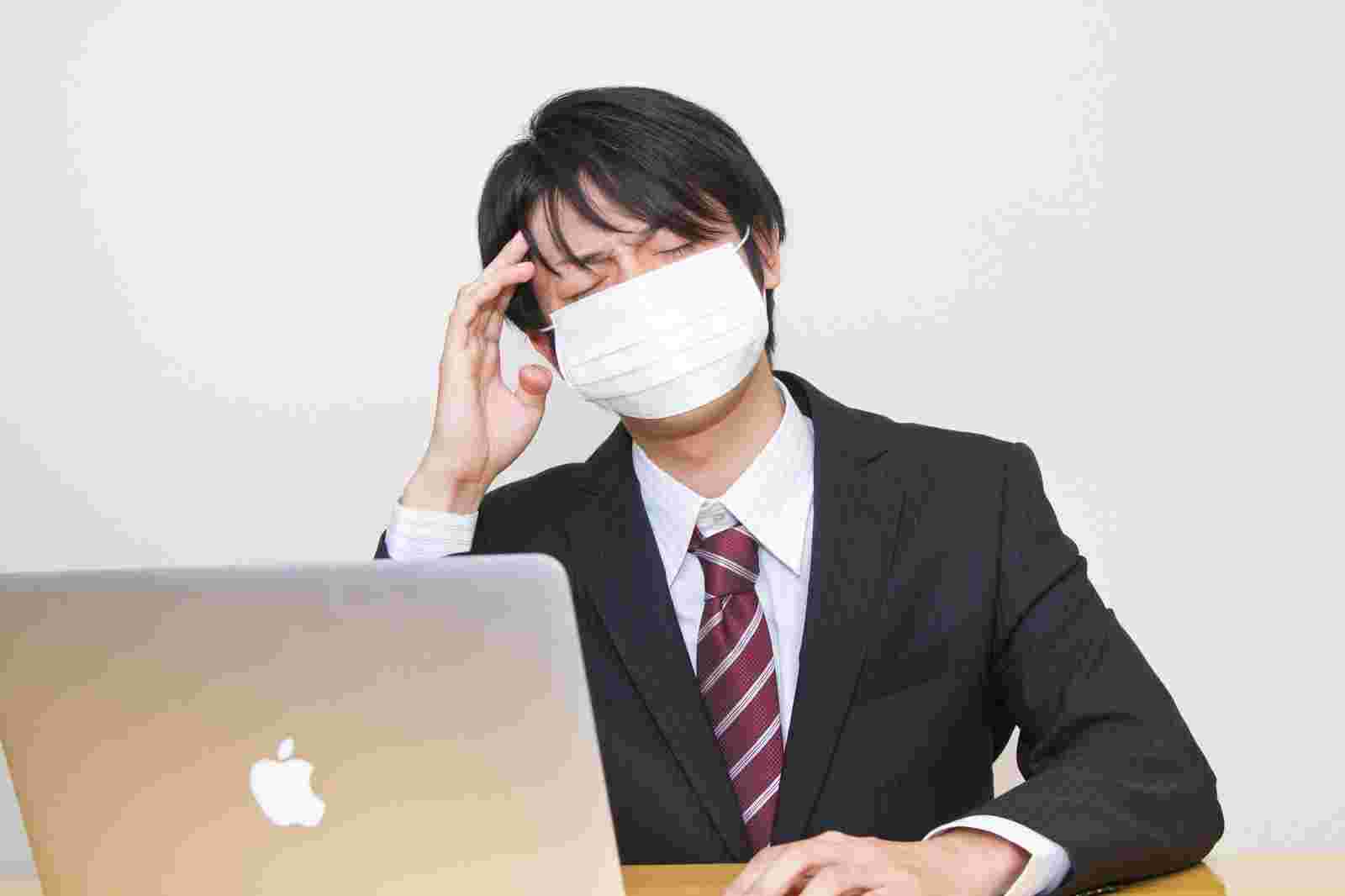 マスク姿でつらそうに仕事をするスーツ姿の男性