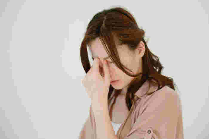 眉間に手を当てつらそうにしている女性