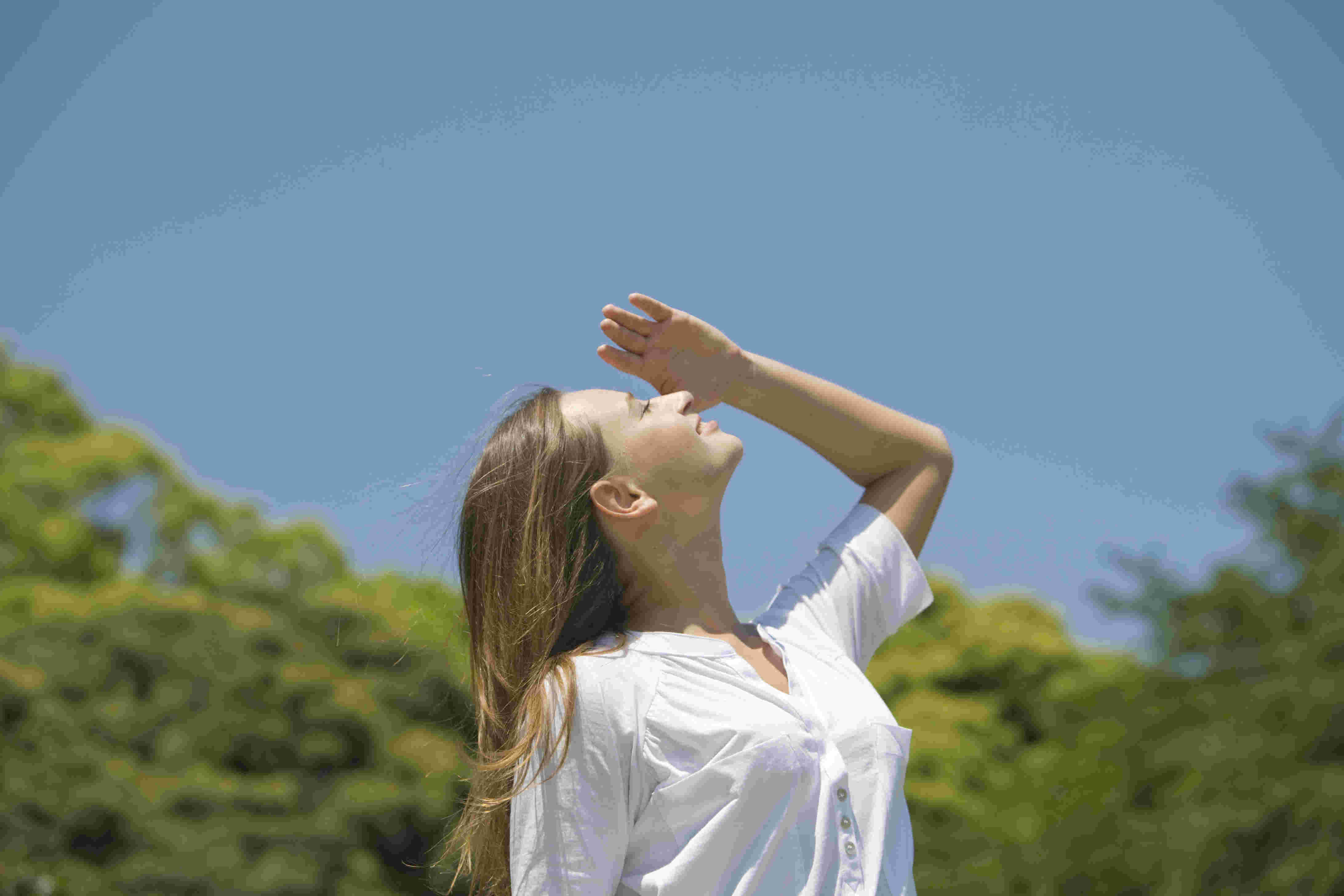 手を顔に当ててまぶしそうに空を見上げる女性