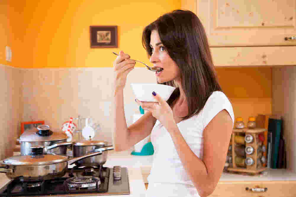 出来立てのスープをキッチンで立ちながら味見する女性