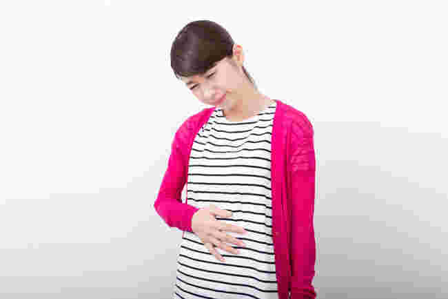 お腹を押さえて顔をしかめる女性