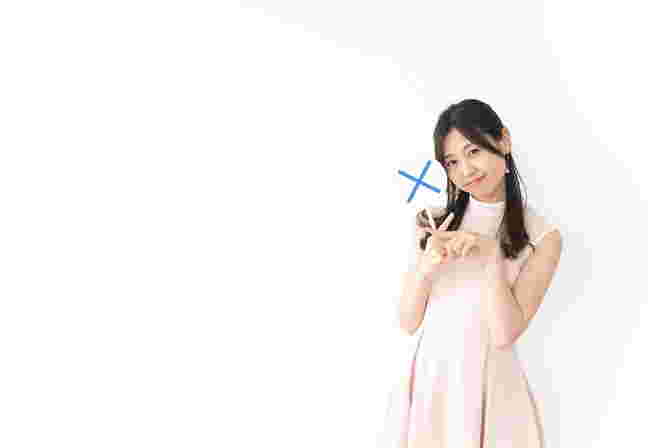 バツ印を手に持ちバツマークをつくる女性