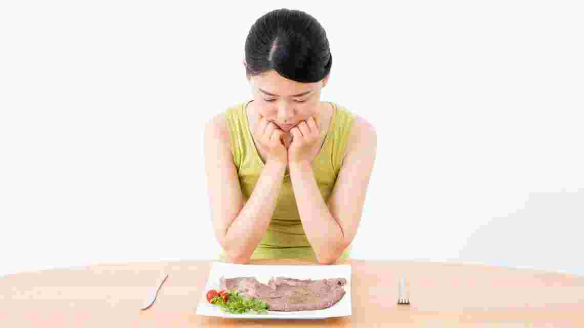 肉のステーキを目の前に考え込む女性