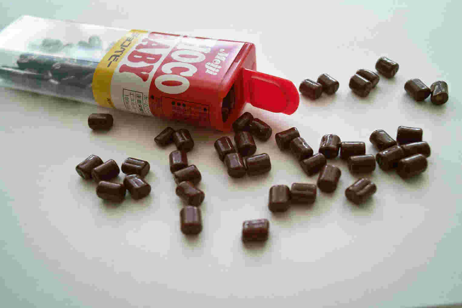 細長い筒の蓋が開き、小粒のチョコがたくさん散りばめられている