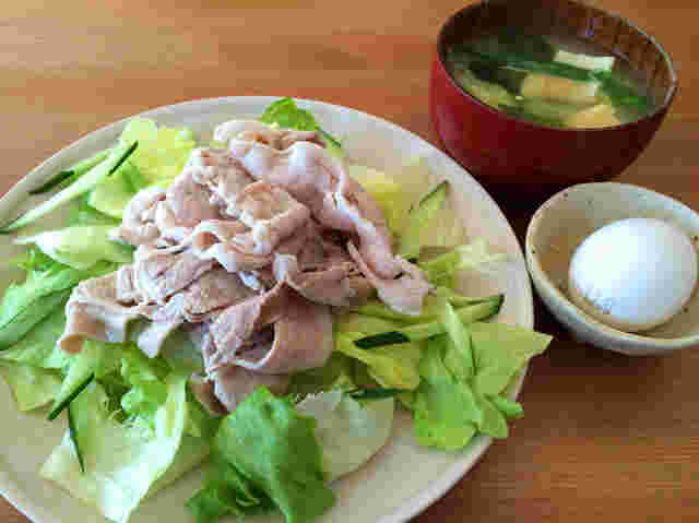 丸いお皿の上に野菜と肉が盛り付けられ、味噌汁と小さい器に玉子が入れられている