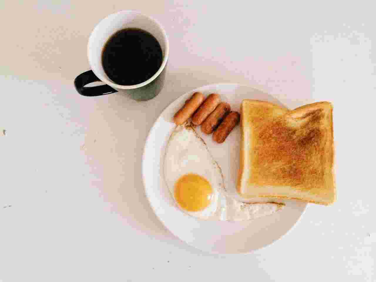コーヒーが注がれたカップと丸いお皿の上に目玉焼き、焼かれたパン、ウィンナー4本が置かれている