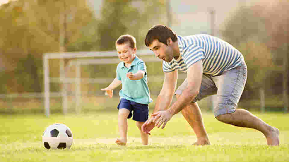 大きな広場で男性と子供が裸足でサッカーボールを追いかけている