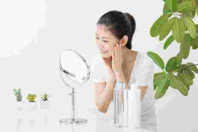 鏡を見て微笑みながら化粧水をつける女性