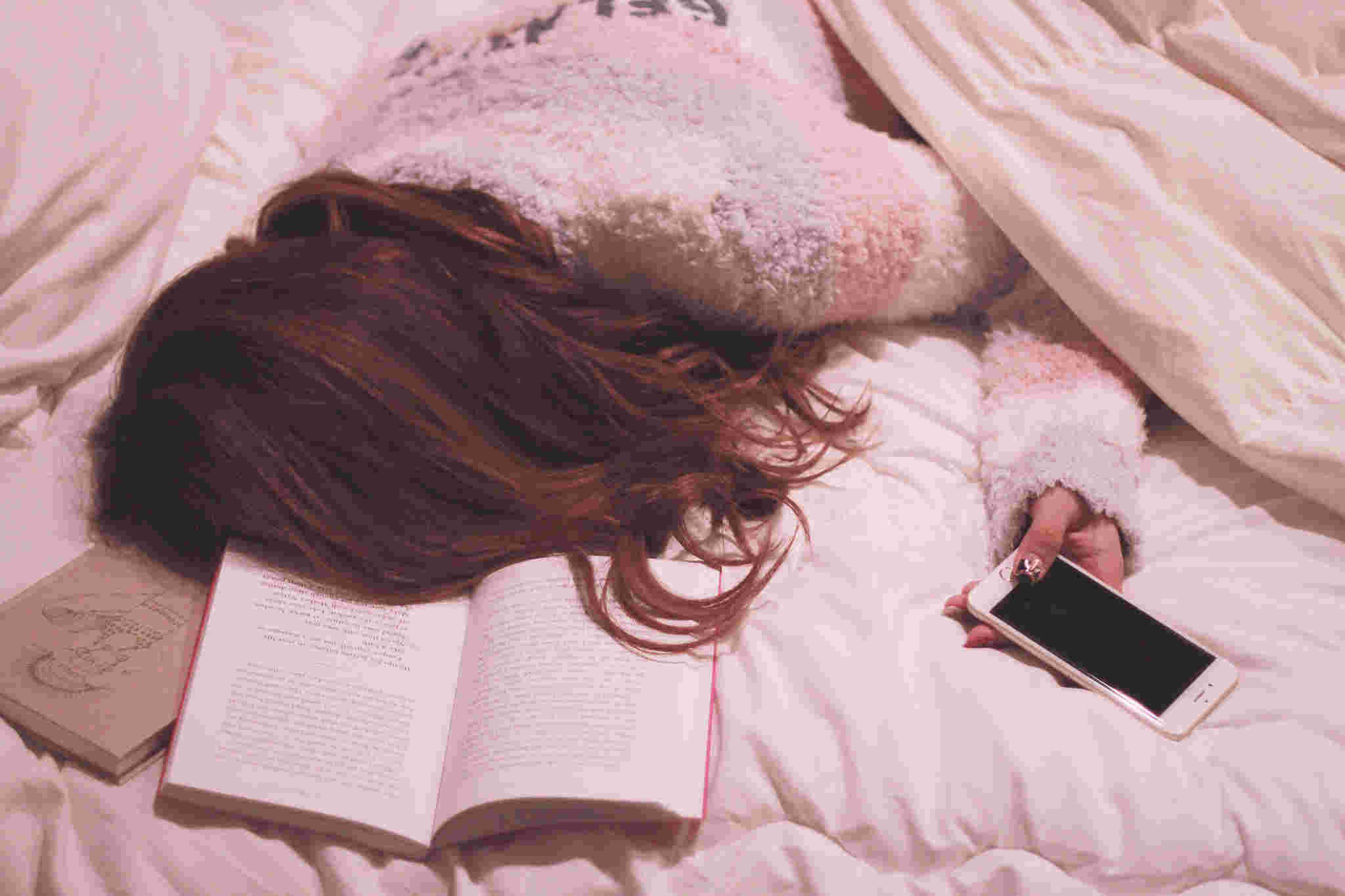 ベッドの上で本を開きながらスマホ片手に寝落ちしてしまった女性