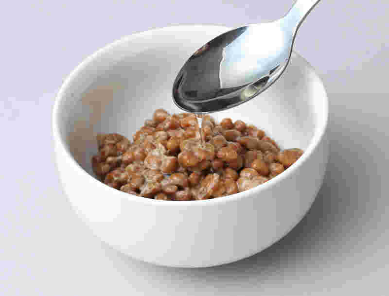お皿に入った納豆にお酢をスプーンで入れている様子