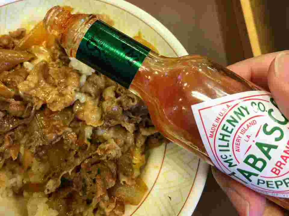 牛丼にタバスコを振りかけている様子