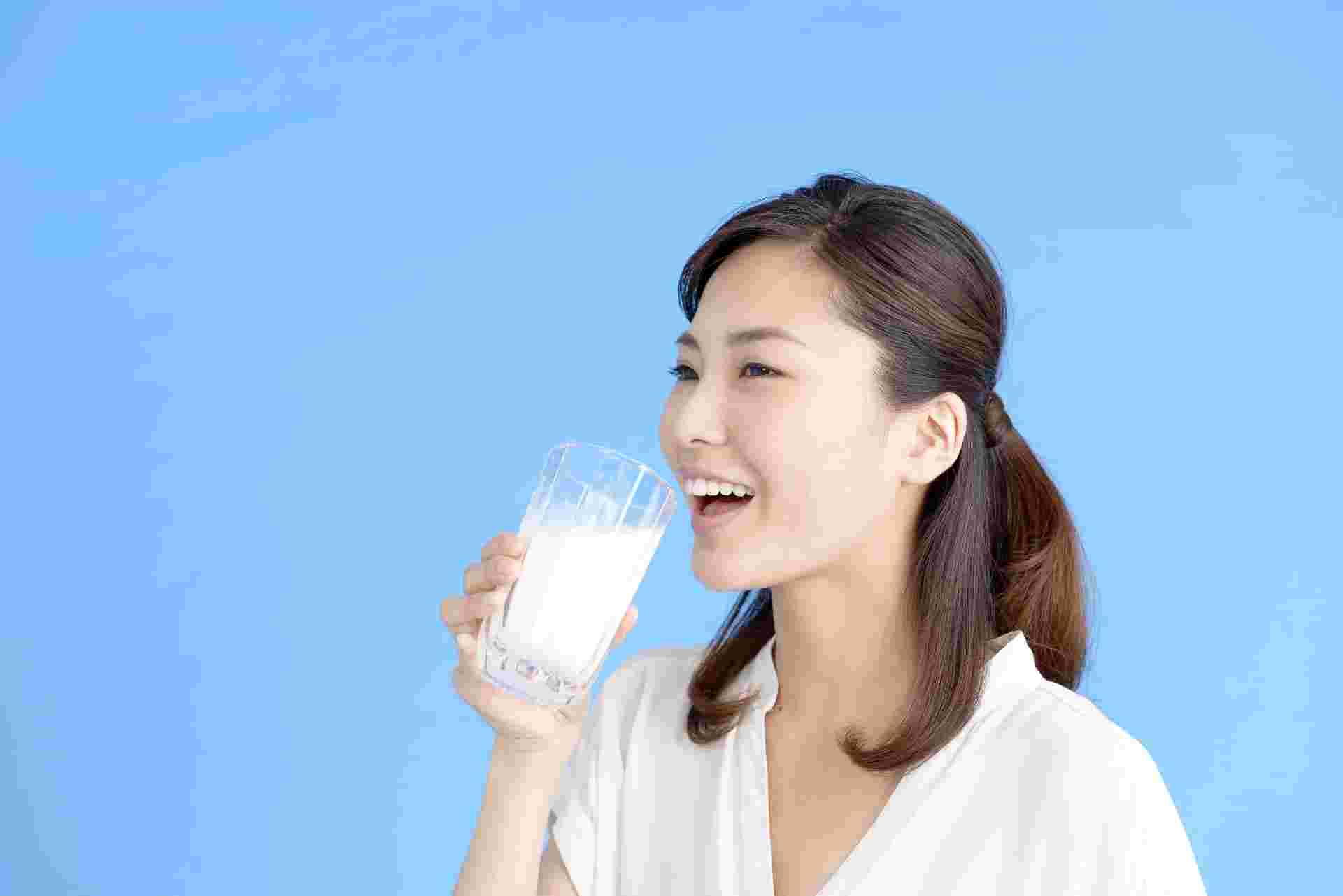 笑顔でガラスのコップに入った牛乳を手に取る女性