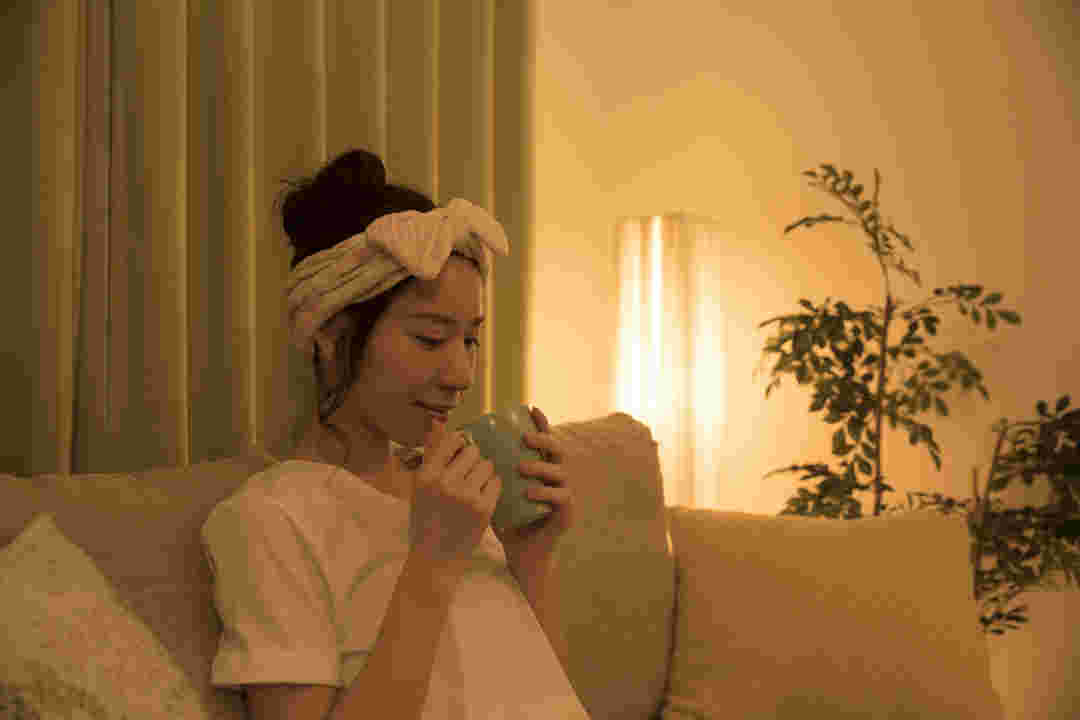 夜、ソファーでくつろぎながらコップを手に取る女性