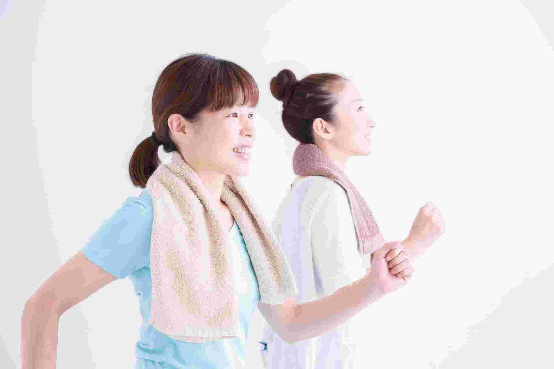 室内でタオルを首に巻いて運動する2人の女性
