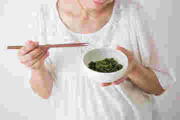 青菜の胡麻あえの器を手に持ち、箸を持つ妊婦さん
