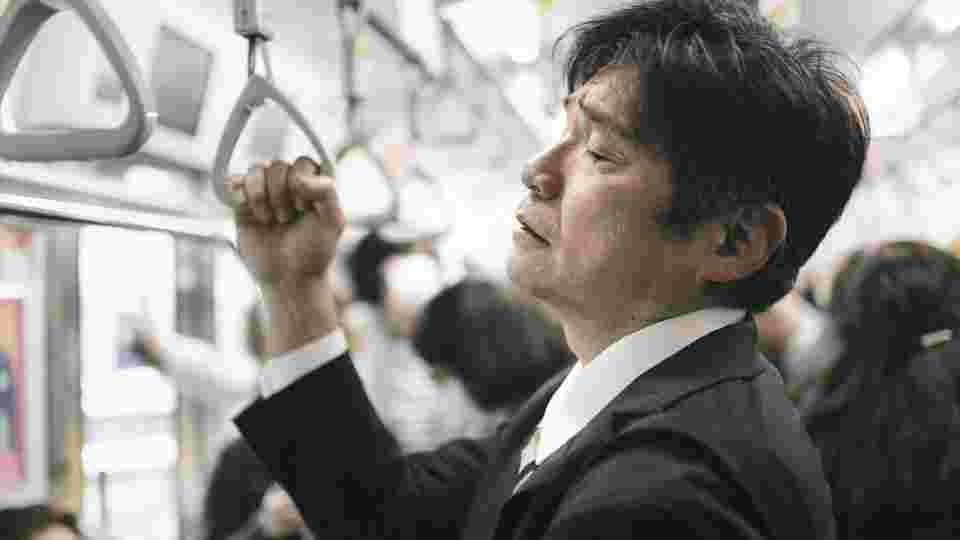 過労で電車のつり革につかまる男性