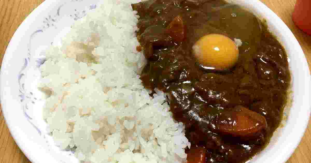 丸いお皿に白米半分、濃ゆそうなカレーのルーが半分と生卵が盛り付けられている