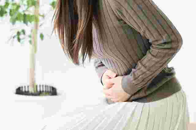 ベージュのニットに白いスカートの女性がお腹をおさえる
