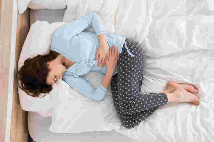 お腹を押さえてベッドによこたわる女性