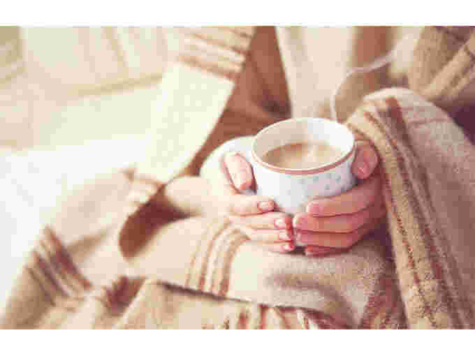 女性が毛布にくるまってコーヒーカップを両手で持っている様子