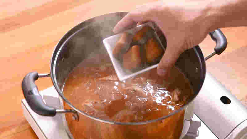 深みのある丸い鍋にスープを煮込み、手にカレーのルが入った皿で入れようとしている