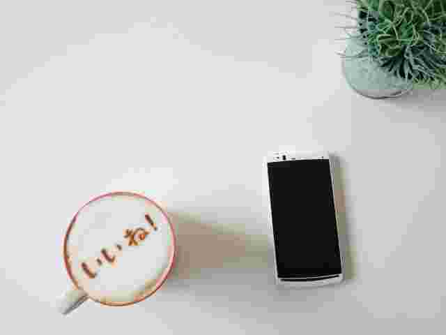 いいねと書かれたカプチーノとスマホと観葉植物