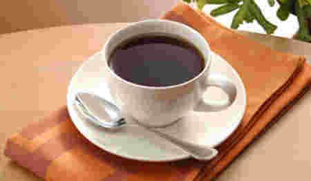 白いカップに注がれてスプーンを添えた深煎りコーヒー