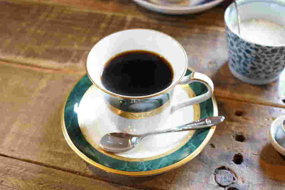 上品なグリーンと白のカップに注がれた深煎りコーヒー