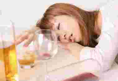 二日酔いで倒れている女性とアルコールのグラスが3つ並んでいる様子