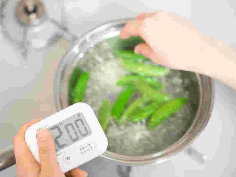 キッチンタイマーを持ちながらスナップエンドウを茹でる