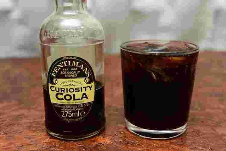 木製の台にキュリオスティコーラのボトルとグラスに入ったコーラ