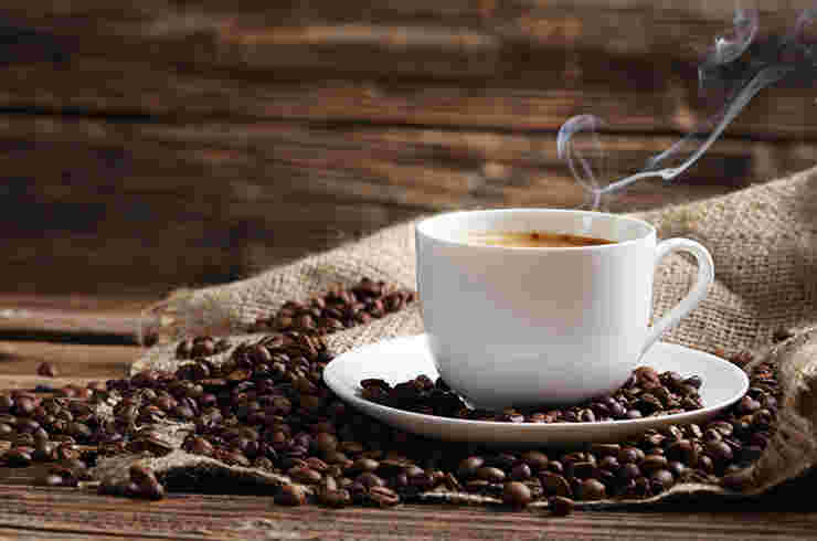白いカップに注がれて湯気を出している熱々のコーヒーと、大量に散らばったコーヒー豆